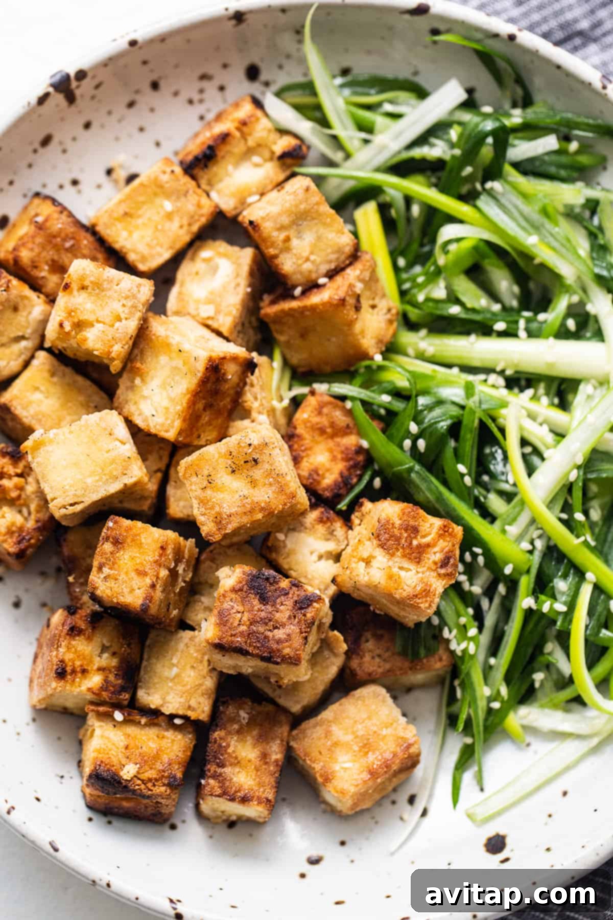 A plate of freshly pan-fried crispy tofu, garnished and ready to eat.
