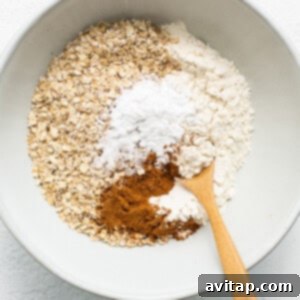Oats and cinnamon in a bowl with a wooden spoon, part of the dry ingredients for the baked oatmeal.