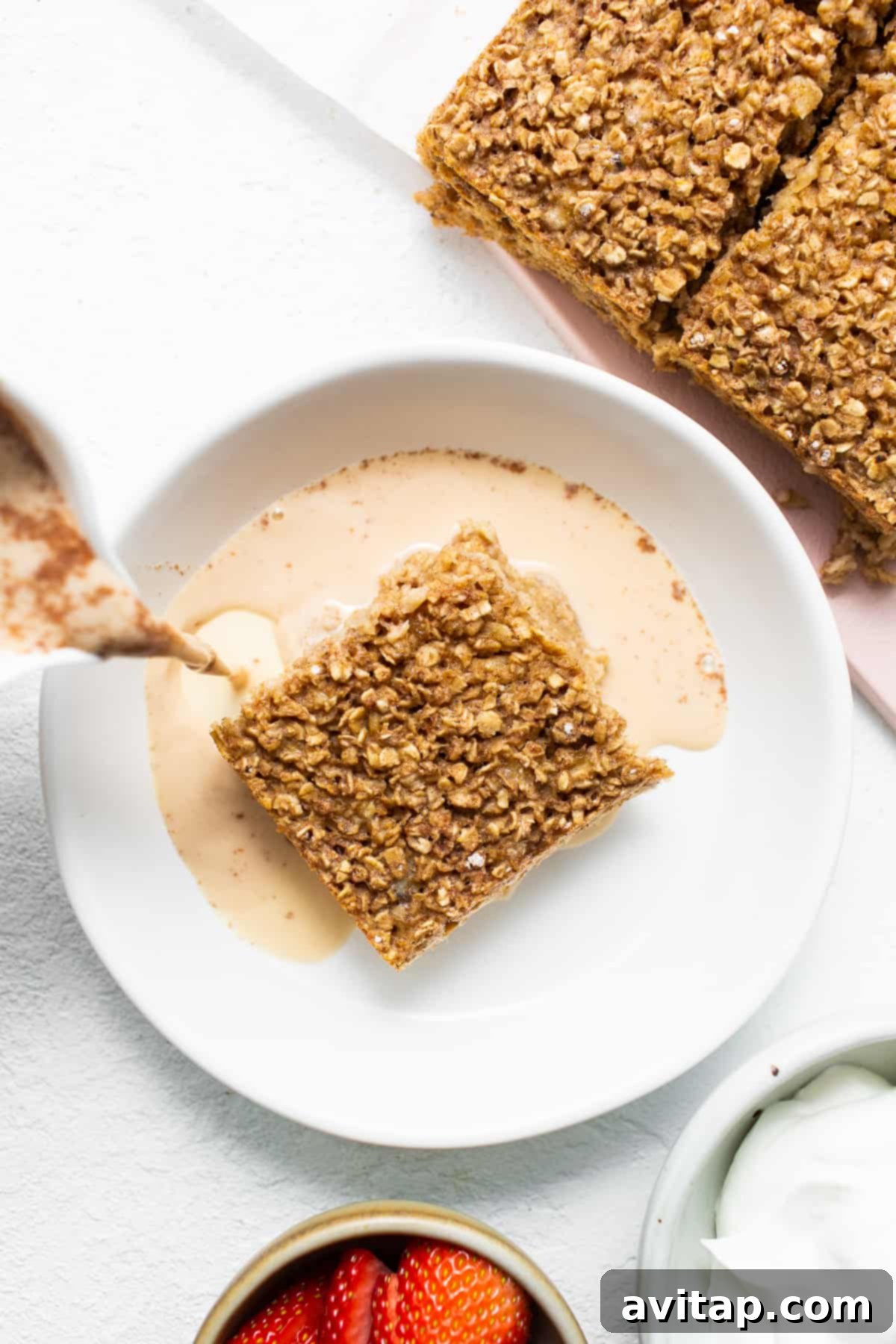 A perfectly portioned slice of warm tres leches baked oatmeal resting on a clean white plate, ready for immediate enjoyment. The golden top and moist interior are visible.