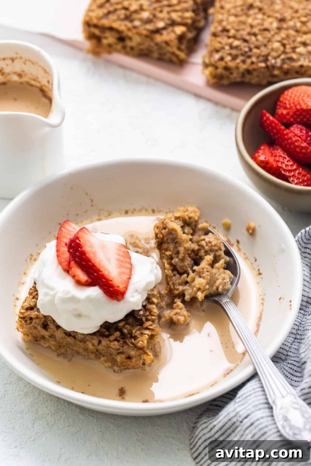 A stunning close-up of a generous slice of tres leches baked oatmeal, elegantly adorned with a luxurious swirl of fresh whipped cream and a scattering of vibrant red strawberries.