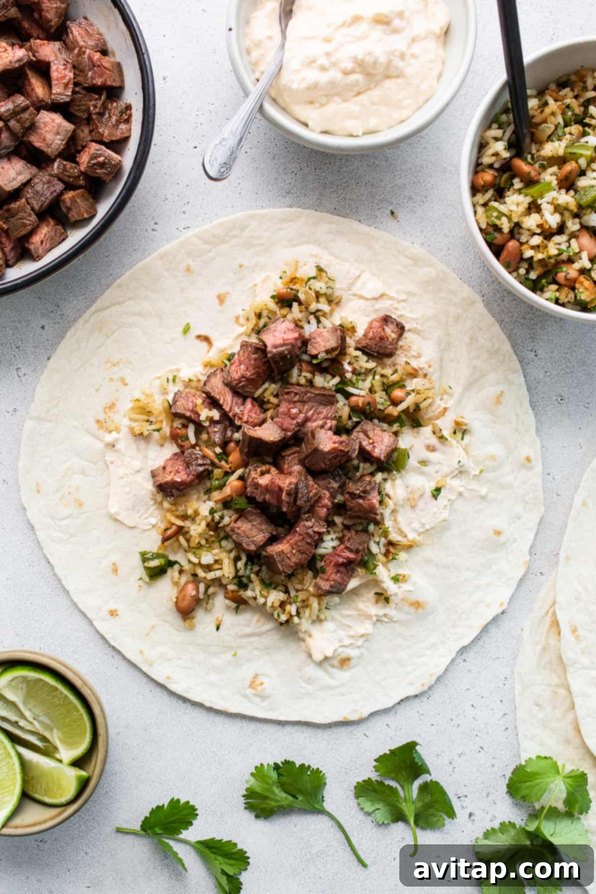 A disassembled steak burrito, with neatly diced steak, vibrant rice and vegetable mixture, and a dollop of creamy sauce laid out on a large flour tortilla on a wooden cutting board, ready for rolling.
