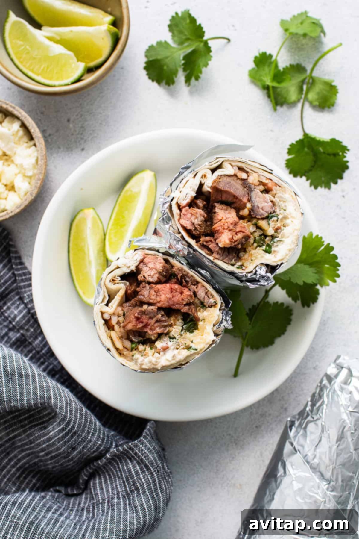 A vibrant steak burrito, unwrapped and cut in half, revealing its rich filling of steak, rice, beans, and cheese, served on a plate with fresh lime wedges and cilantro for garnish.