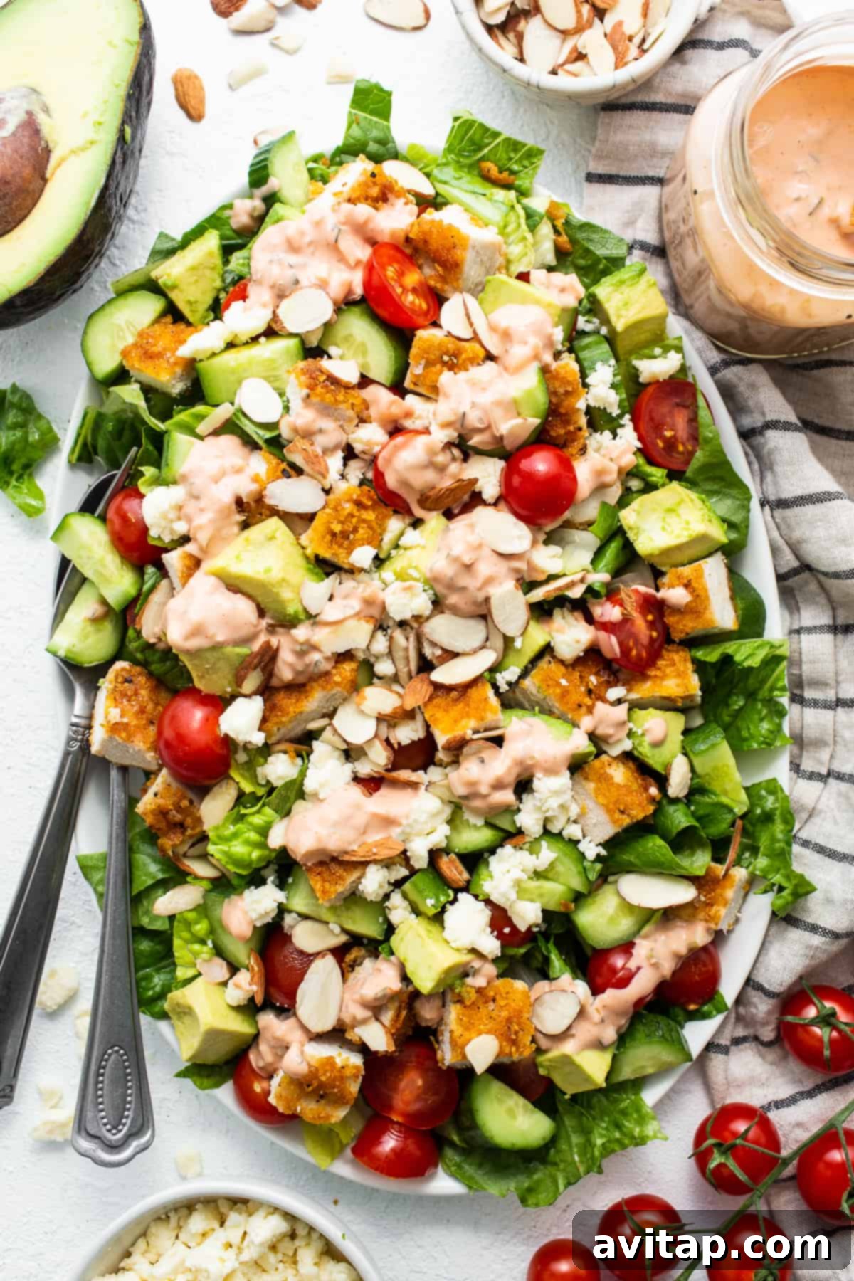 A vibrant crispy chicken salad with cornflake-crusted chicken, fresh greens, cherry tomatoes, and avocado, drizzled with creamy dressing.