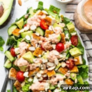 A salad with chicken, tomatoes, avocado and dressing on a plate.