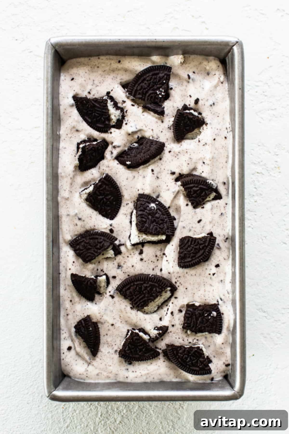 A loaf pan filled with smooth, white cottage cheese ice cream mixture, sprinkled with crushed Oreos, ready to be frozen.