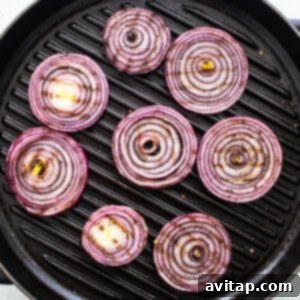 Red onion rings grilling on an outdoor grill.