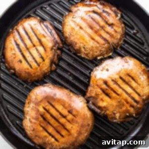 Four grilled portobello mushroom caps in a grill pan.