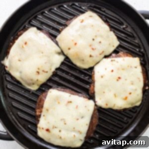 Four portobello cheeseburgers with melted cheese in a grill pan.