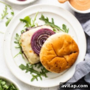 A plate of assembled portobello burgers with red onions and arugula.