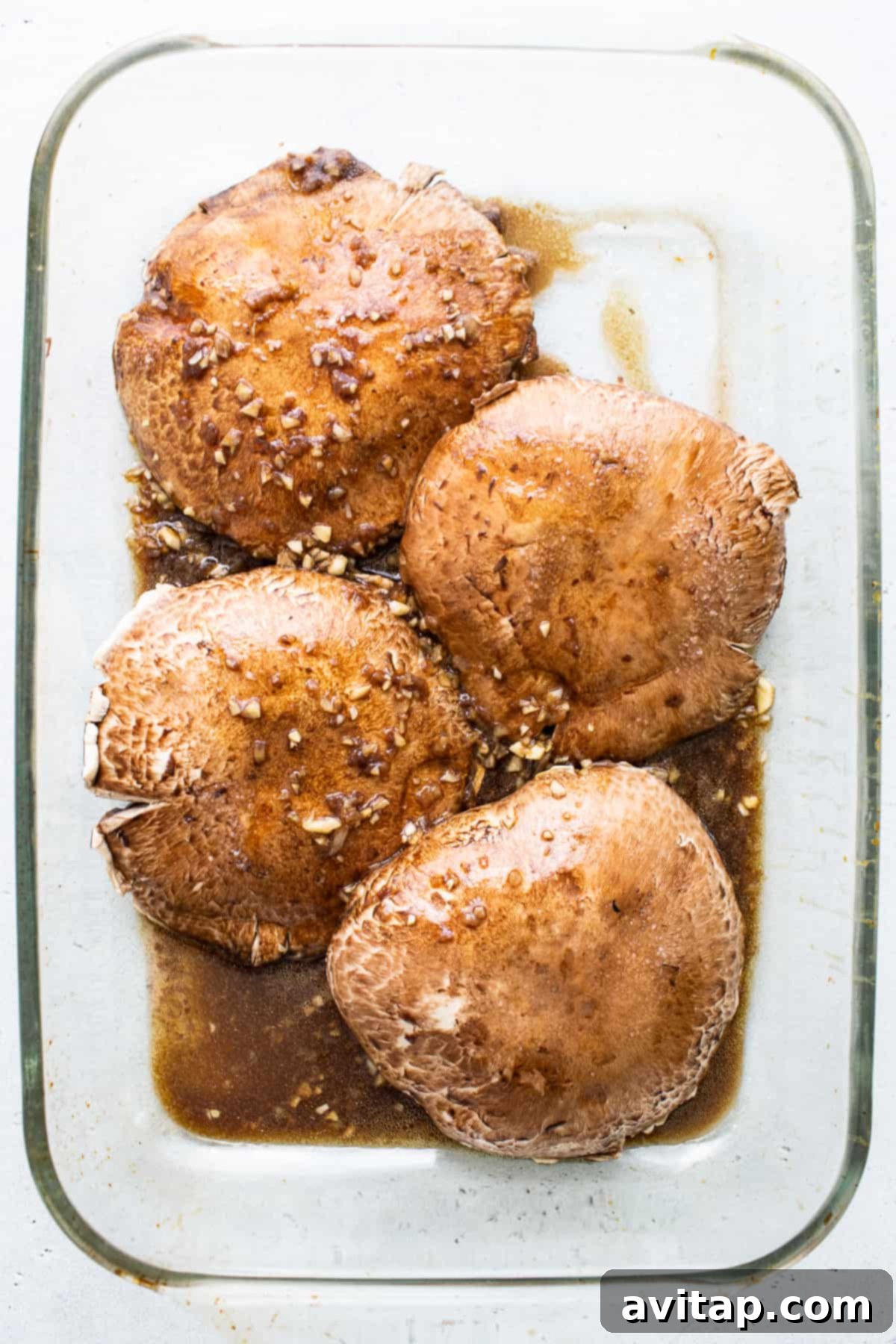 Close-up of portobello mushroom caps thoroughly coated in a flavorful marinade, ready for grilling.