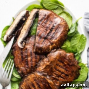 A plate of perfectly grilled portobello mushrooms garnished with fresh spinach and herbs.