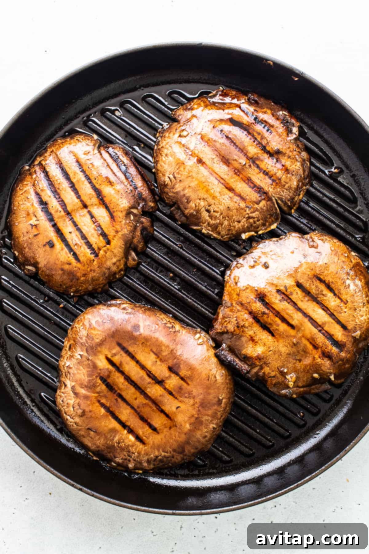 Grilled portobello mushroom caps cooking on a grill pan, showing delicious char marks.