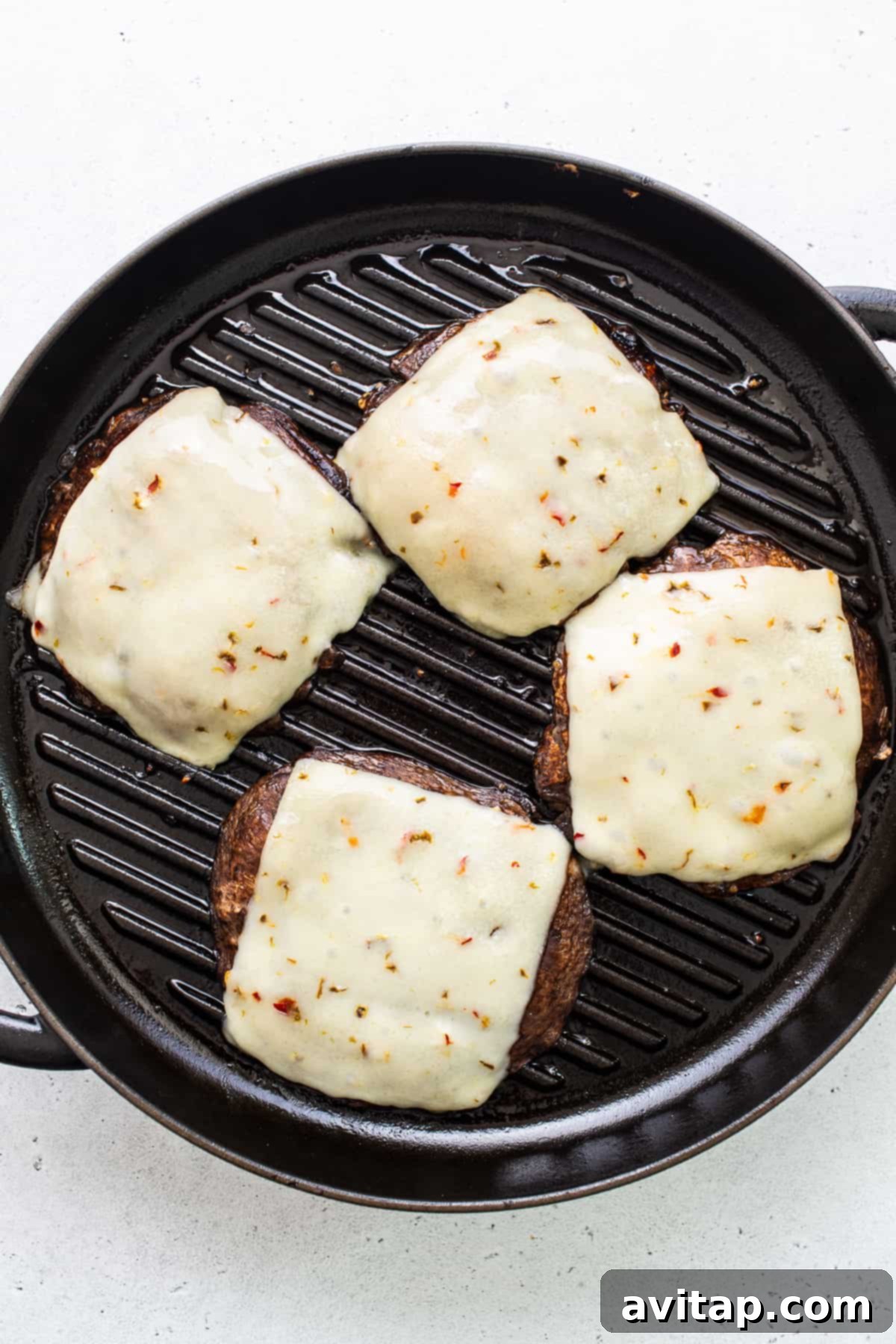 Portobello mushroom burgers with melted pepper jack cheese sizzling in a grill pan, close-up.