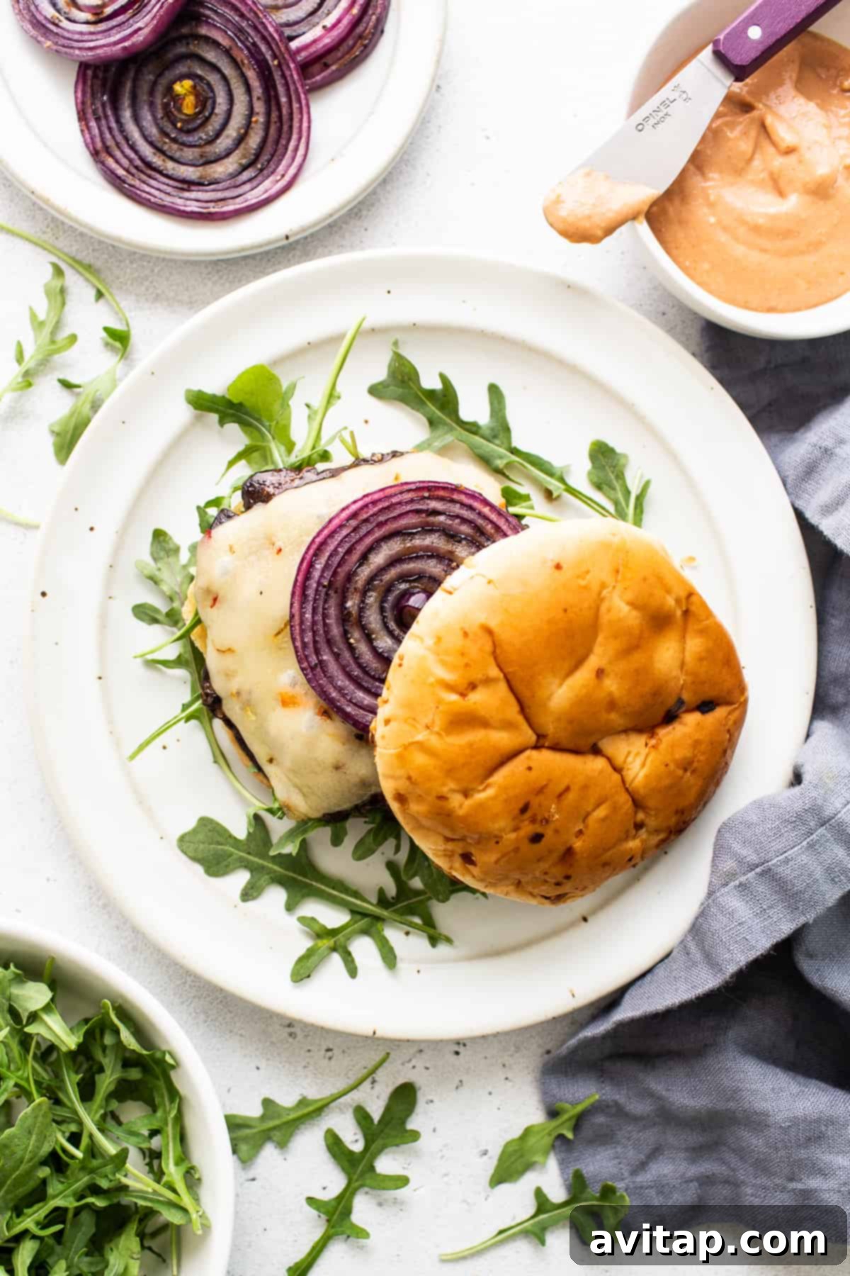 A close-up shot of a gourmet portobello mushroom burger, beautifully assembled with melted cheese, grilled onions, and fresh greens, served on a toasted bun.
