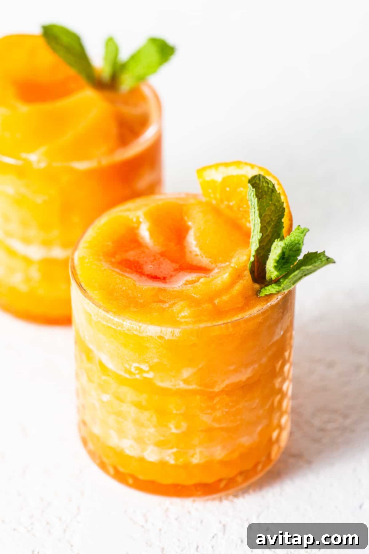 A close-up of a perfectly blended Frozen Aperol Spritz Slushy in a glass, with subtle condensation, an orange slice, and a straw, promising refreshing relief.