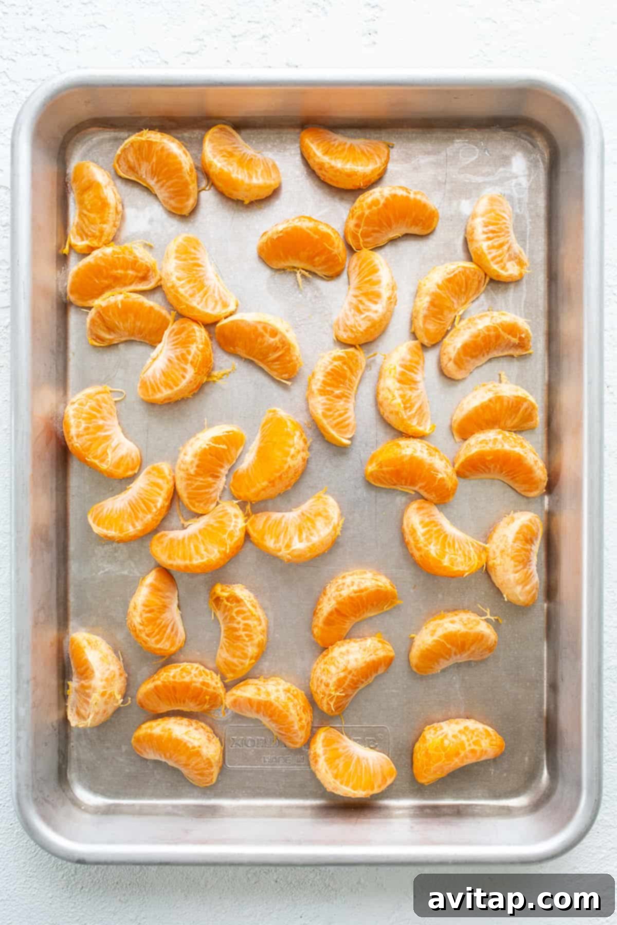 Fresh clementine slices neatly arranged in a single layer on a parchment-lined baking sheet, prepared for freezing to achieve the ideal slushy consistency.
