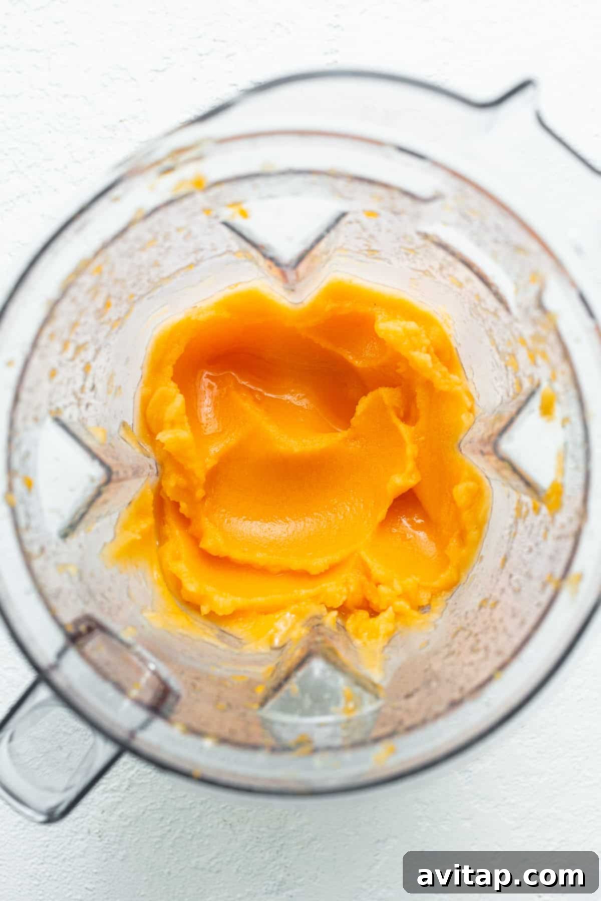 A high-speed blender container filled with the vibrant orange mixture for Frozen Aperol Spritz Slushies, mid-blend, creating a frothy, icy texture.