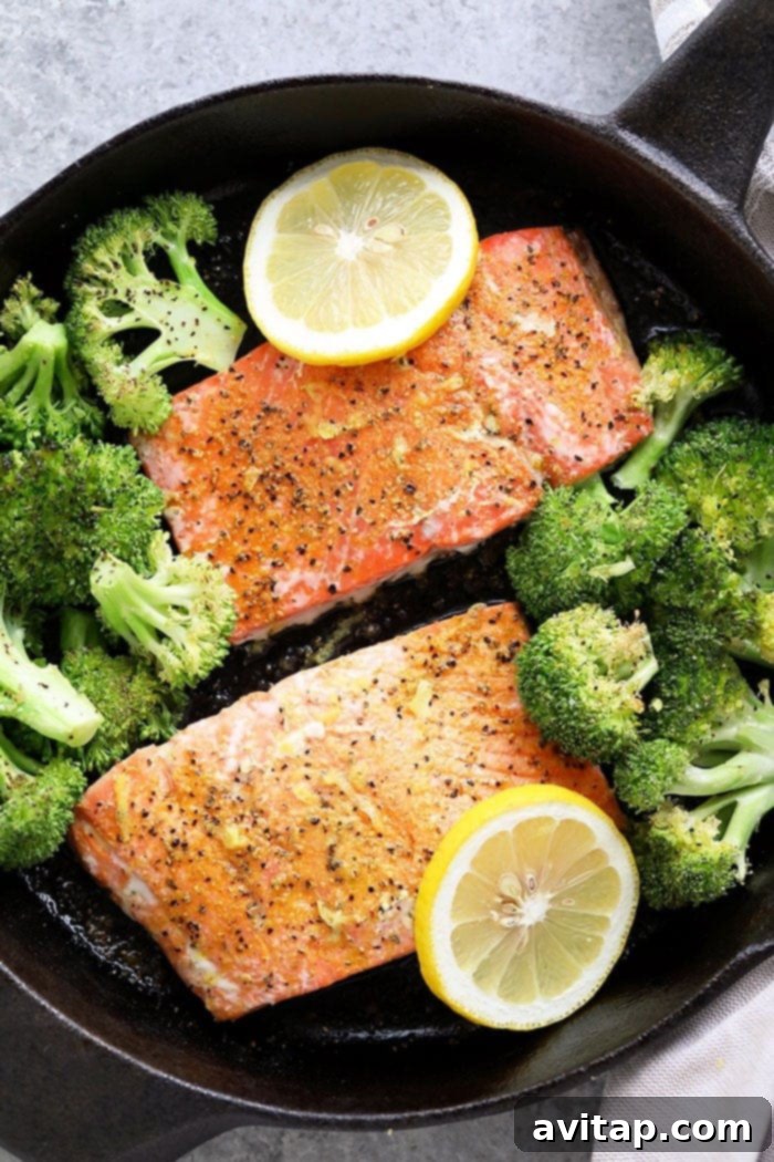 Two perfectly baked lemon pepper salmon fillets, garnished with fresh lemon slices, resting on a bed of roasted broccoli.