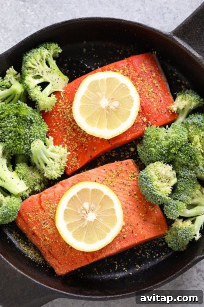 Close-up of a salmon fillet seasoned with lemon pepper and salt, topped with fresh lemon wedges, ready for baking.