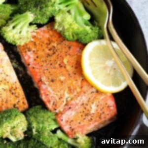 Baked lemon pepper salmon in a cast iron skillet, garnished with fresh lemon.