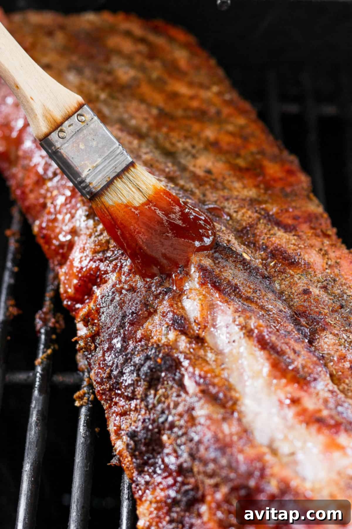A BBQ grill with a spatula coated in barbecue sauce, ready to baste the ribs.