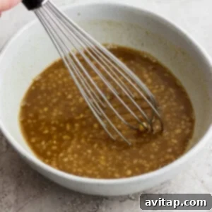 a hand holding a whisk in a bowl of brown liquid.