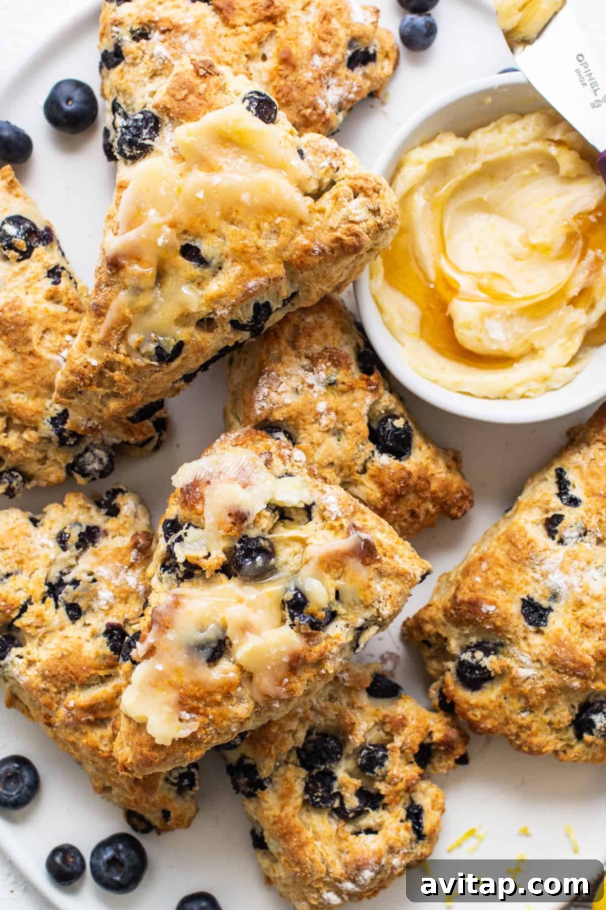 A white plate generously topped with golden-brown lemon blueberry scones and scattered fresh blueberries, ready for breakfast.