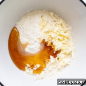 A white bowl filled with flour, milk, almond extract, lemon zest, and blueberries being mixed.