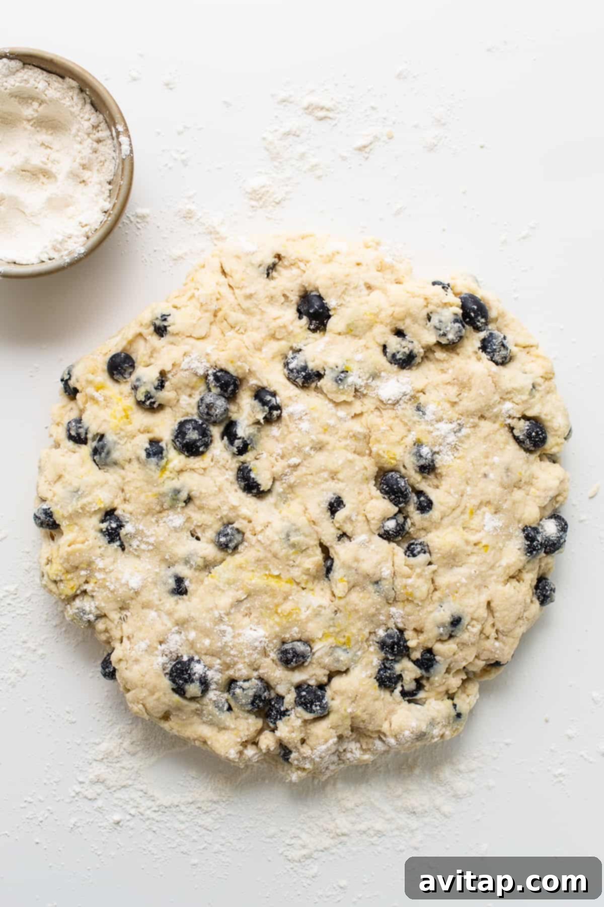 A close-up view of scone dough studded with fresh blueberries and lightly dusted with flour, ready for shaping.