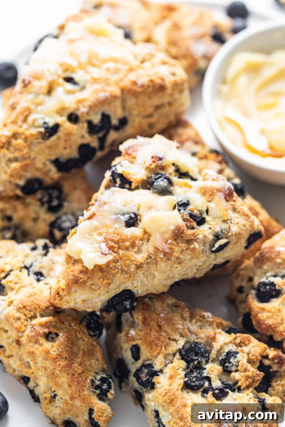 A white plate featuring two golden-brown blueberry scones next to a small bowl of honey butter, ready to be enjoyed.