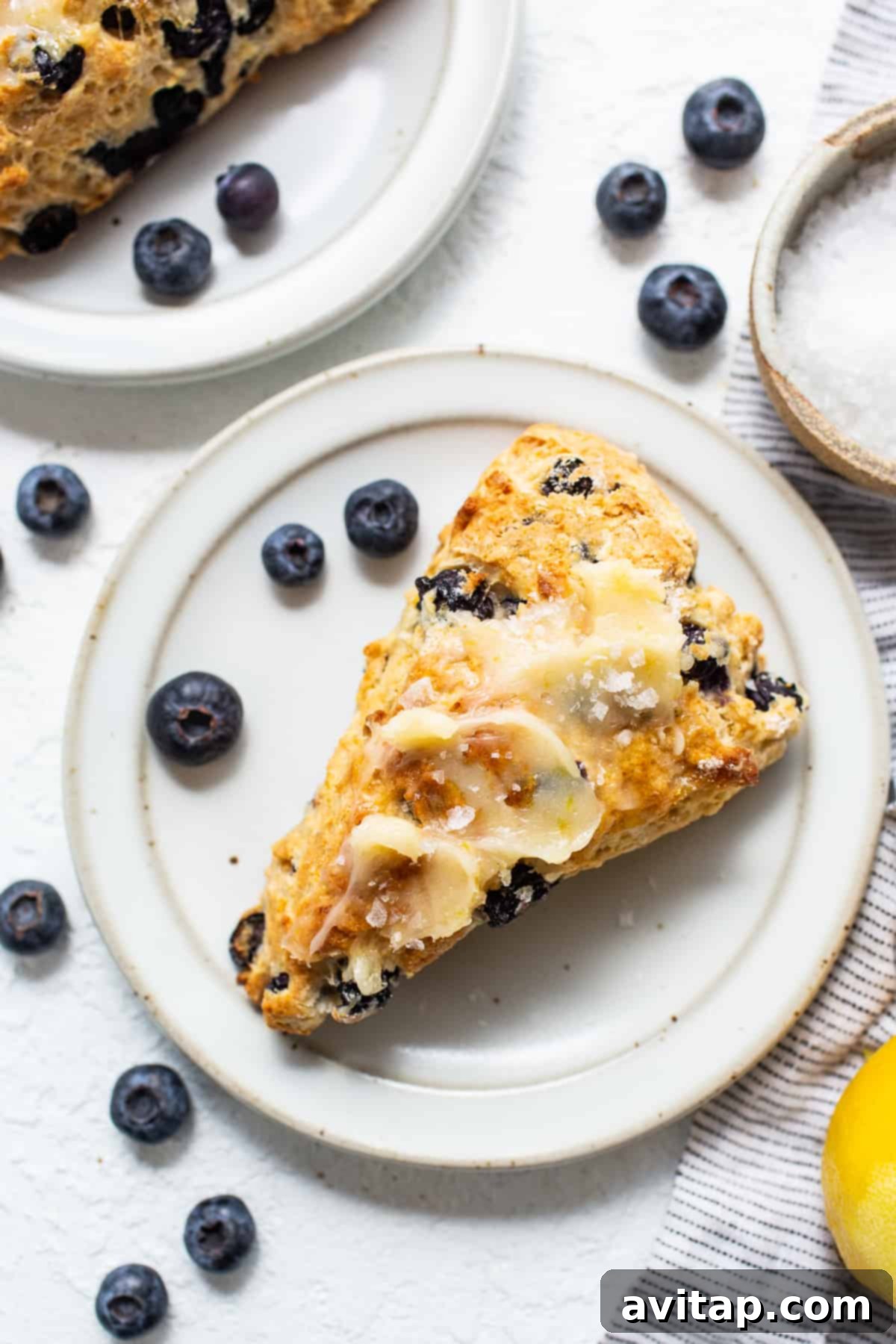 A single slice of a homemade blueberry scone, revealing its tender, flaky interior, rests on a white plate.