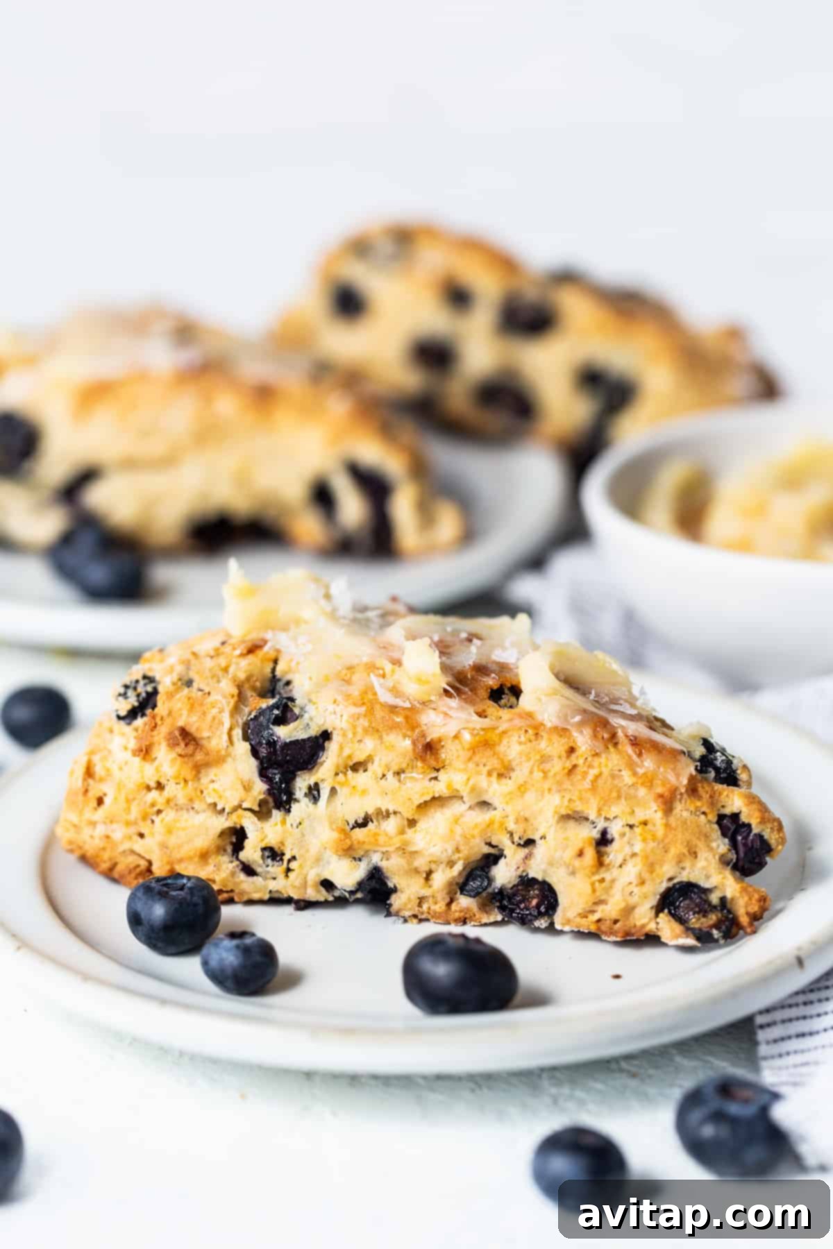 A plate of freshly baked blueberry scones, with one scone having a bite taken out, revealing its soft interior.