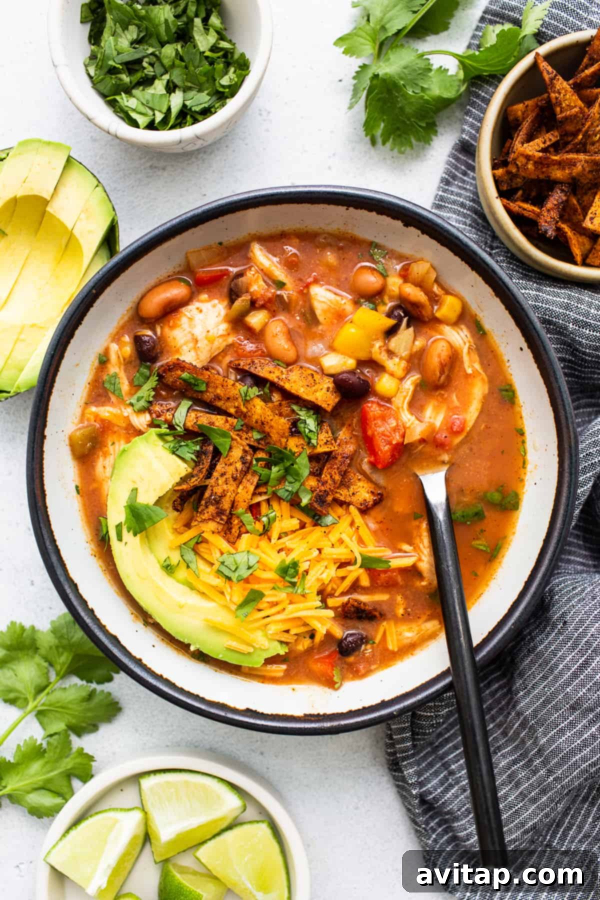 A vibrant bowl of homemade chicken tortilla soup, garnished with crispy tortilla strips, fresh cilantro, and creamy avocado slices.