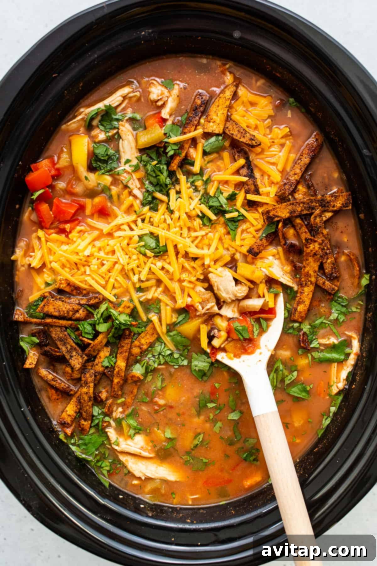 A slow cooker filled with chicken tortilla soup, garnished with fresh cilantro and a lime wedge, ready to be served.