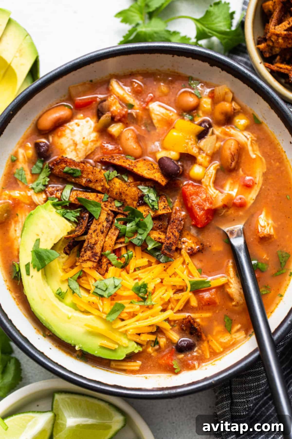 A steaming bowl of chicken tortilla soup, garnished with crispy tortilla strips, fresh cilantro, and a lime wedge, presented on a rustic wooden surface.