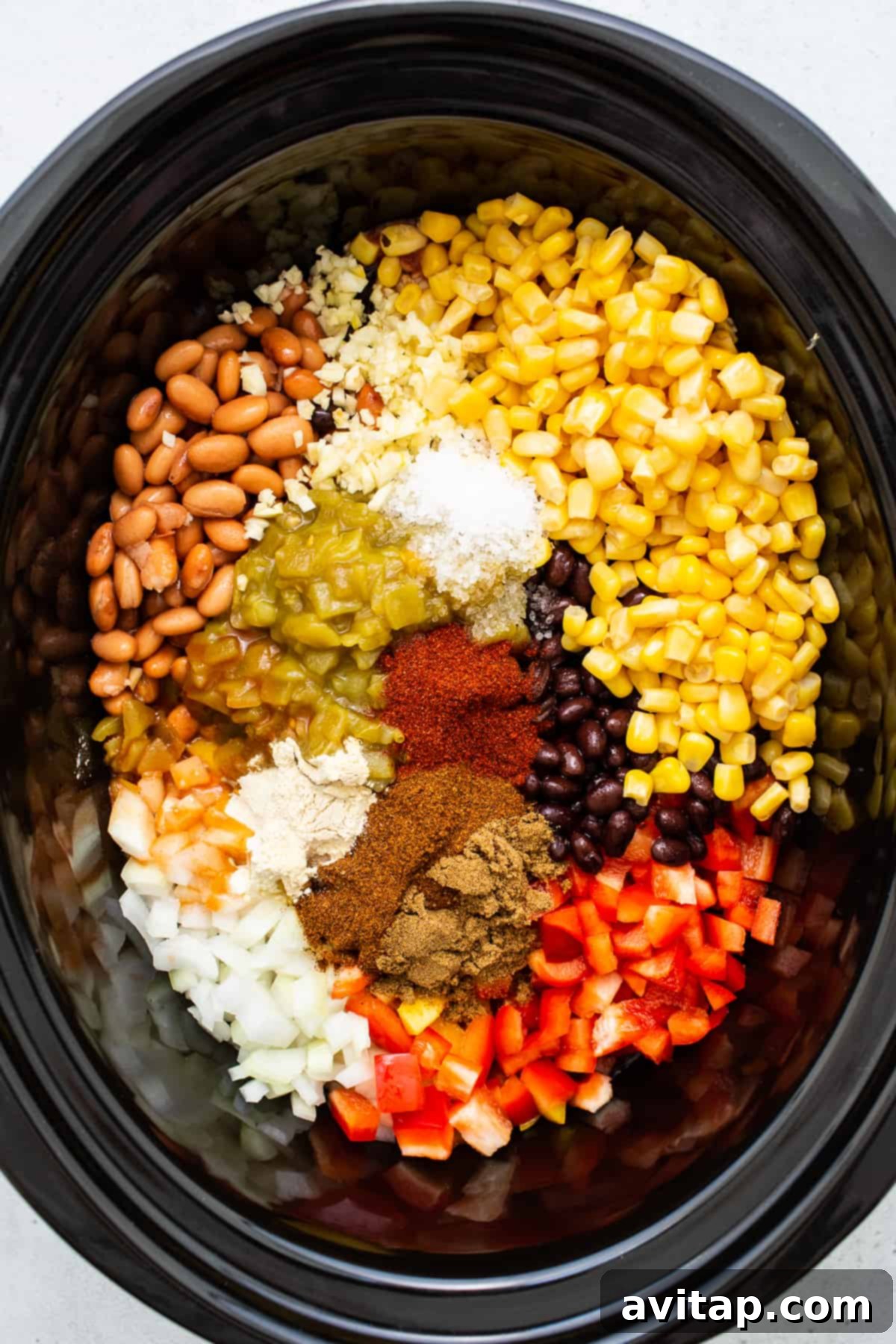 A selection of fresh ingredients for chicken tortilla soup, including chicken breasts, various canned goods, and spices, arranged inside a slow cooker before cooking.