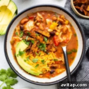 A bowl of Mexican chicken soup with avocado and tortilla chips.