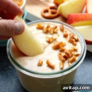 Spiced Pumpkin Yogurt Delight 6 A person is dipping a pretzel into a bowl of pumpkin yogurt dip, highlighting its appeal.