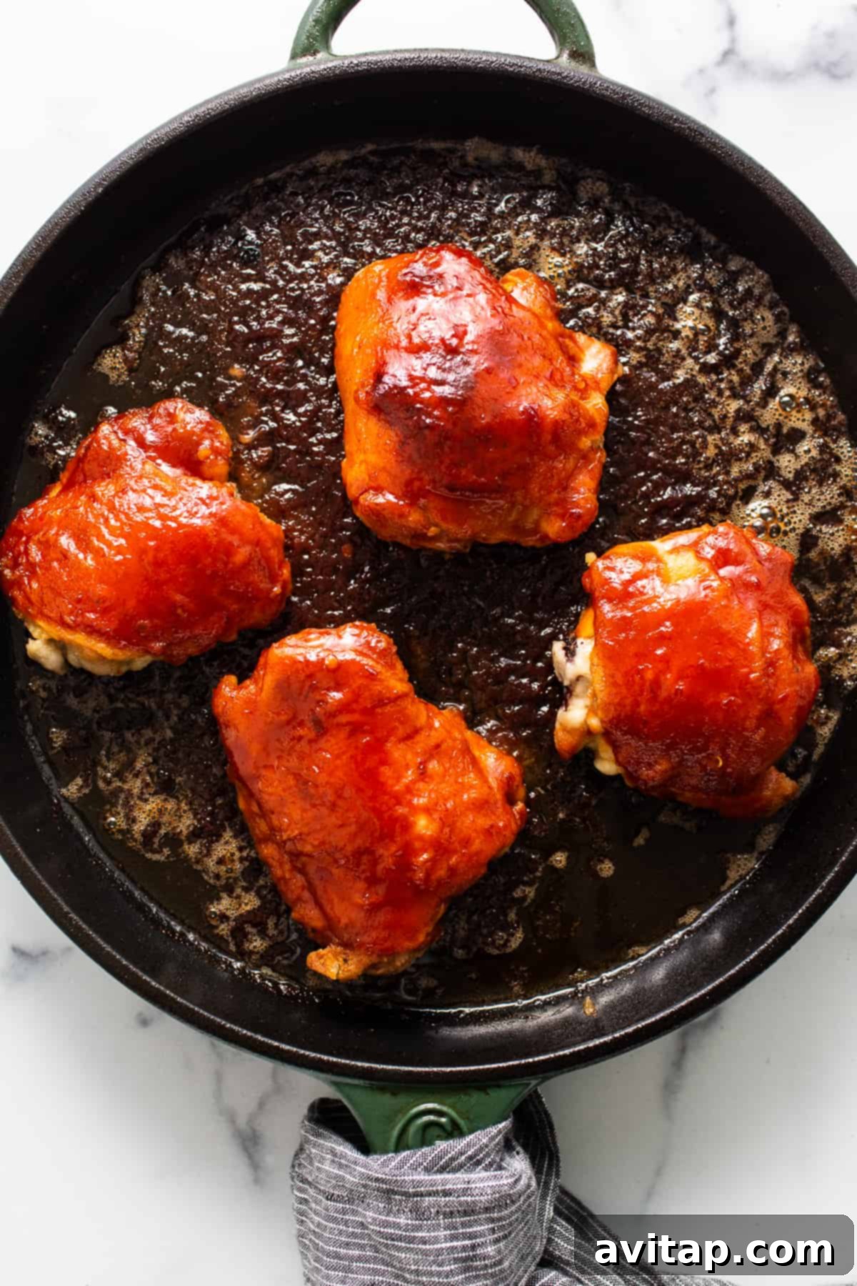 Saucy, glistening chicken thighs simmering in firecracker sauce in a cast iron skillet, fresh out of the oven and ready to be served.