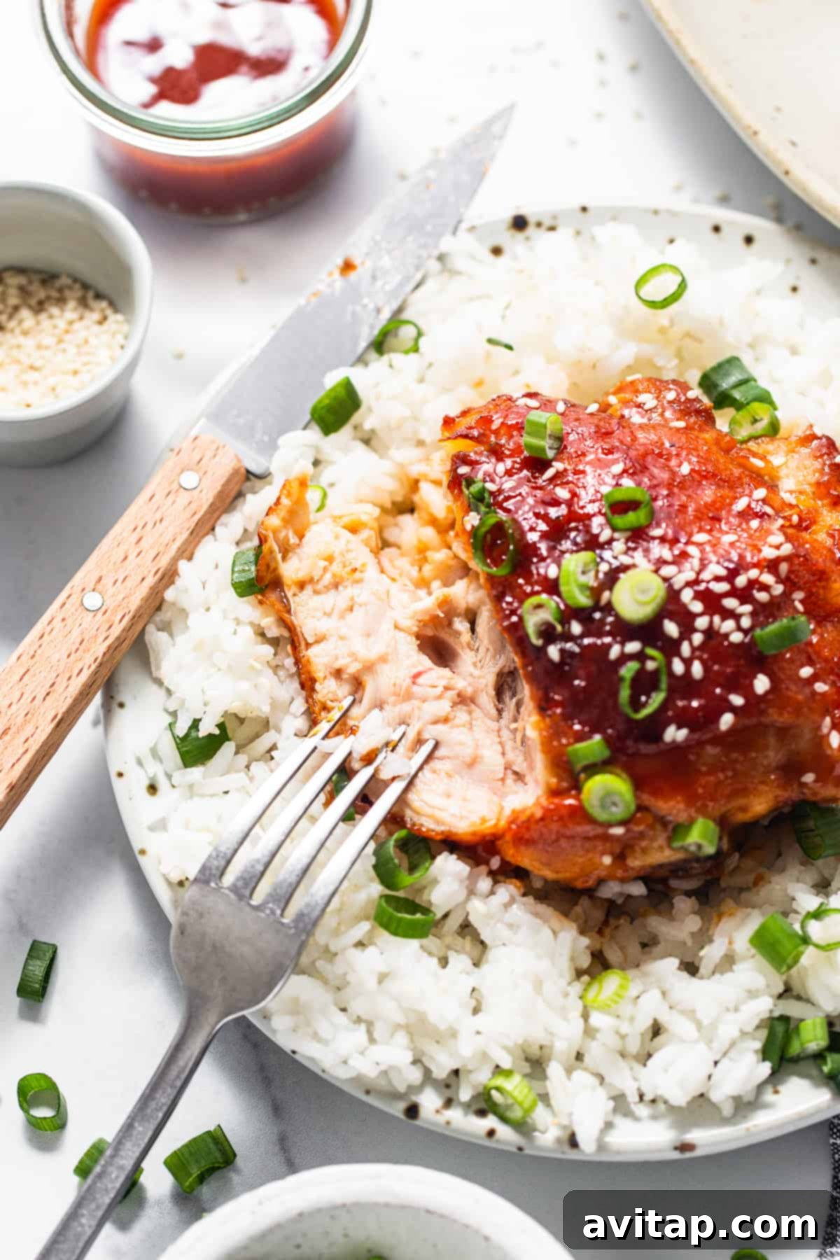 A mouth-watering firecracker chicken thigh on a plate with fluffy white rice and a fork, ready to be enjoyed as a complete meal.