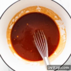 Homemade firecracker sauce in a bowl with a whisk, showing its rich red color and smooth consistency.