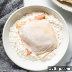 Raw chicken breast coated in a white flour mixture in a bowl, ready for cooking.