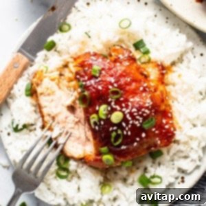 A perfectly cooked firecracker chicken thigh on a plate with fluffy white rice, garnished with green onions and sesame seeds, ready to be enjoyed.