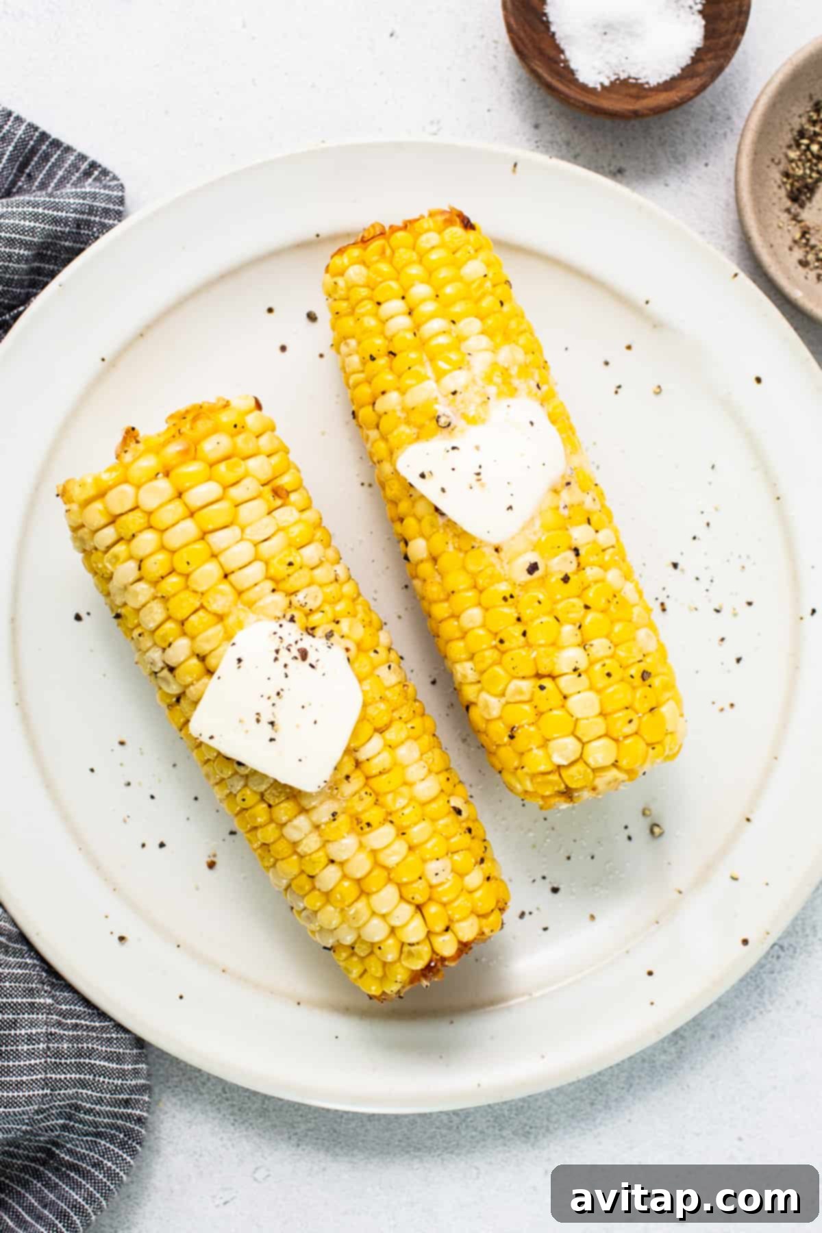 Two corn on the cob with butter on top, ready to be served.