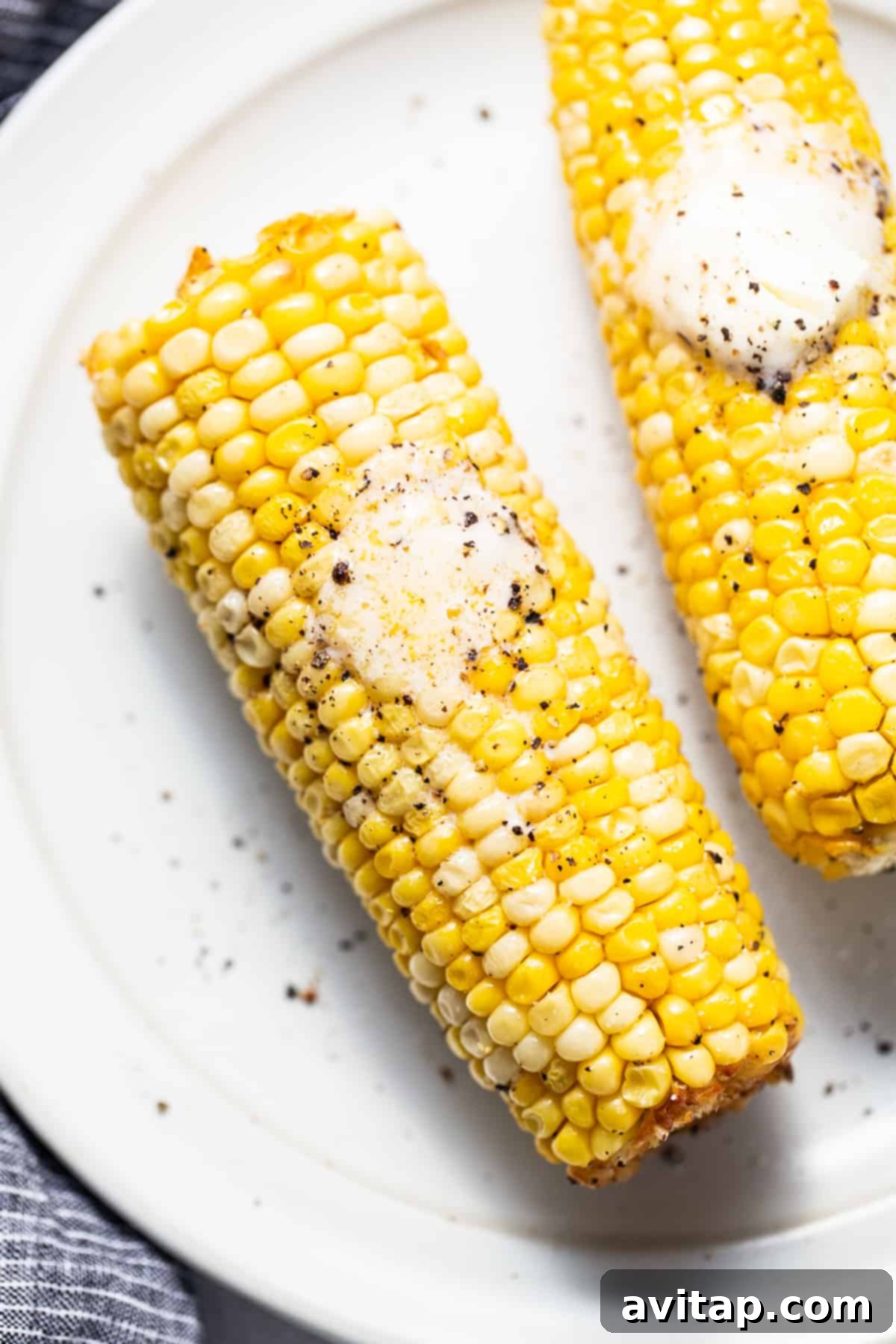 Two corn on the cob resting on a pristine white plate.