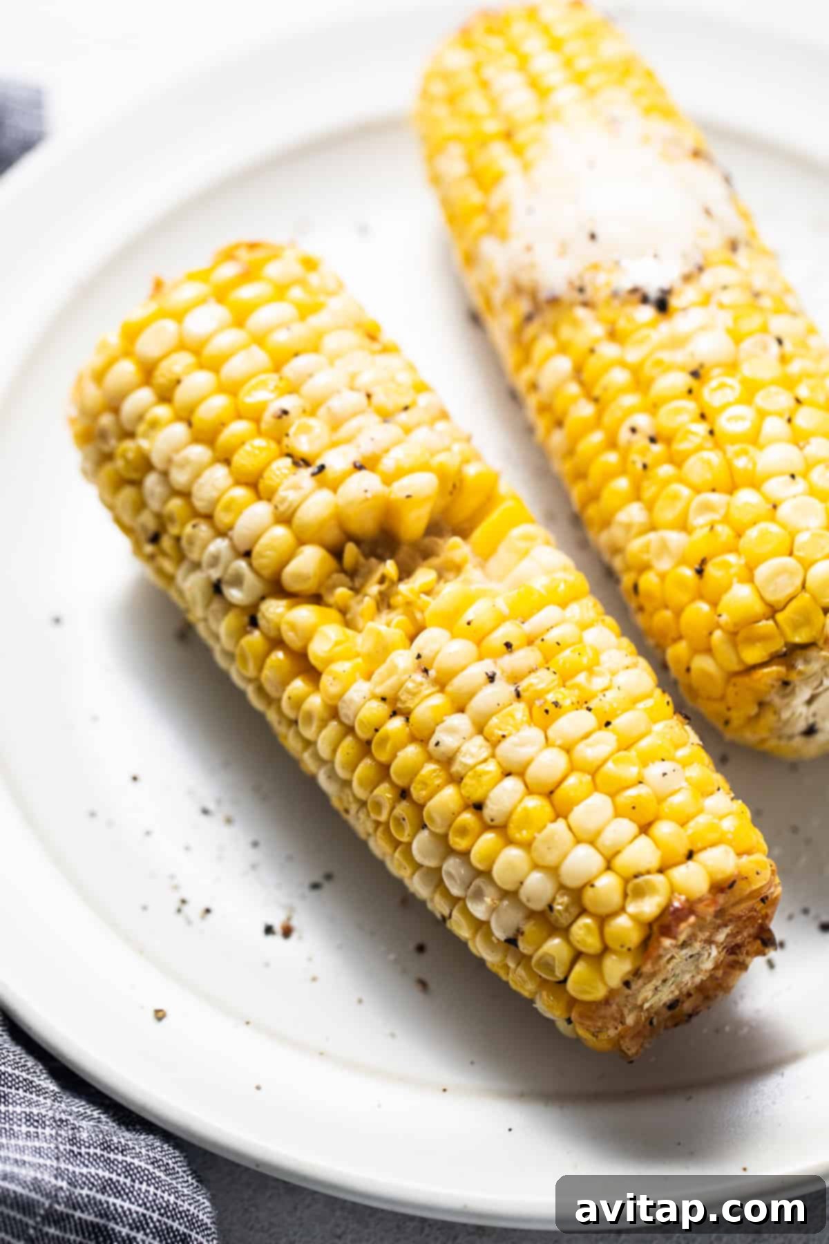 Two corn on the cob on a white plate, showcasing their perfect golden hue.