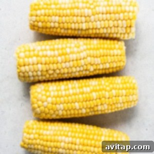 Three ears of corn on a white surface, seasoned and ready for the air fryer.