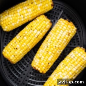 Corn on the cob cooking in an air fryer basket.