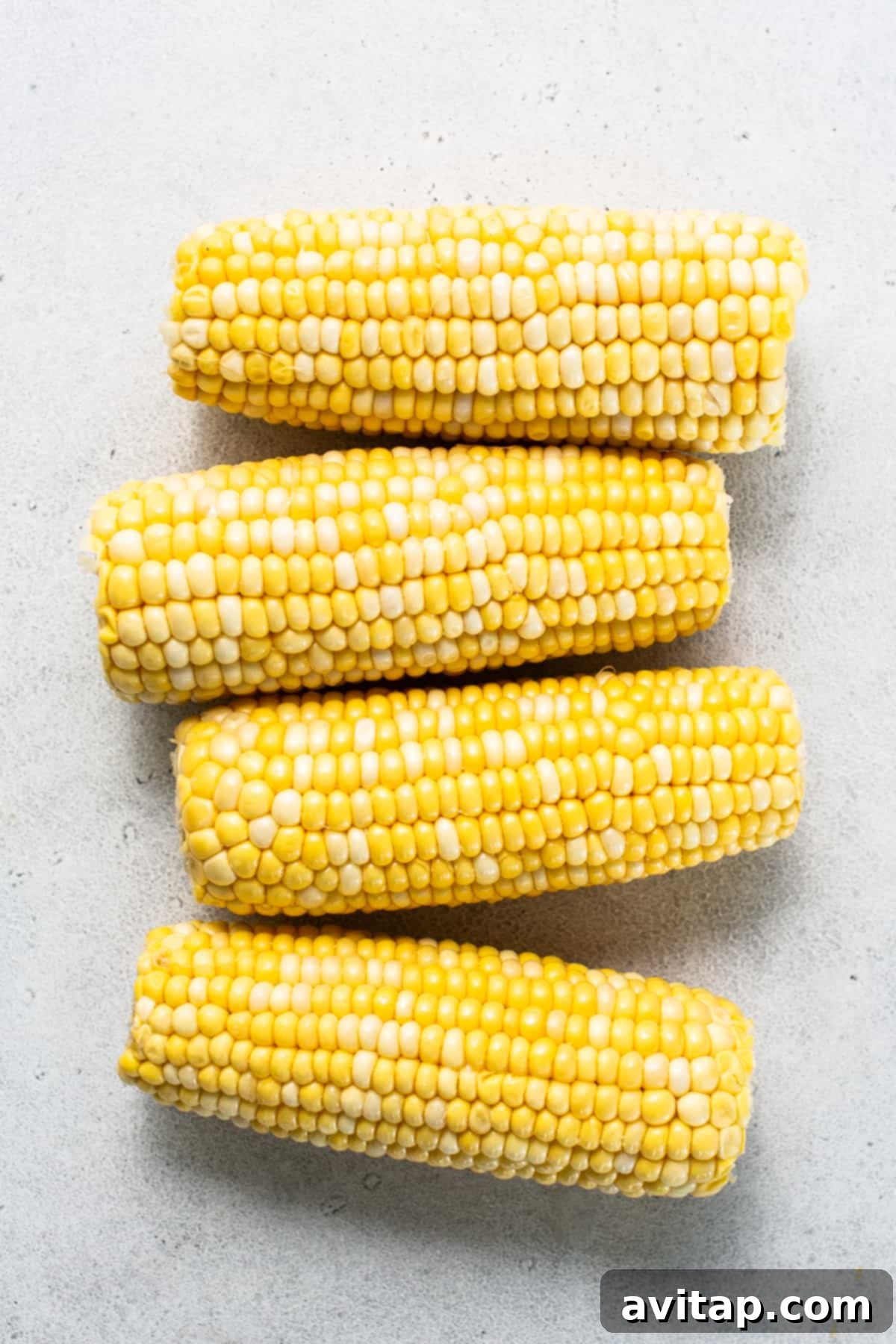 Three ears of corn on a white surface, freshly shucked and ready for seasoning.