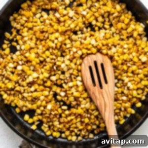 corn in a skillet with a wooden spoon.